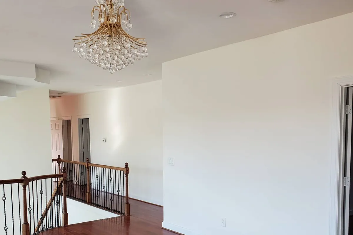 Empty upstairs landing with white walls, cherry hardwood floor, wrought-iron stair railing and crystal chandelier
