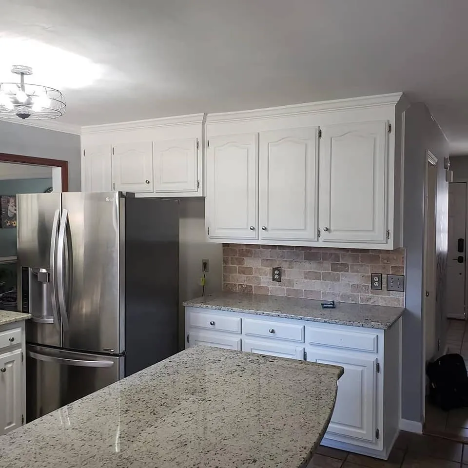 White refinished kitchen cabinets with granite countertops, stone backsplash, and stainless steel refrigerator