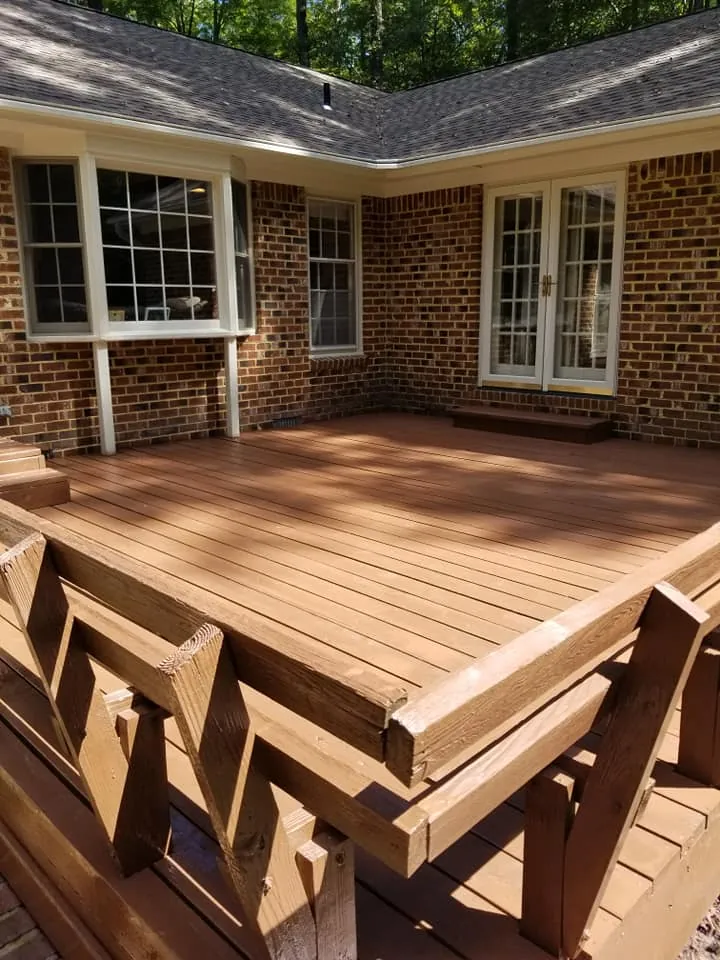 Backyard deck stained medium brown against brick house with French doors and bay window
