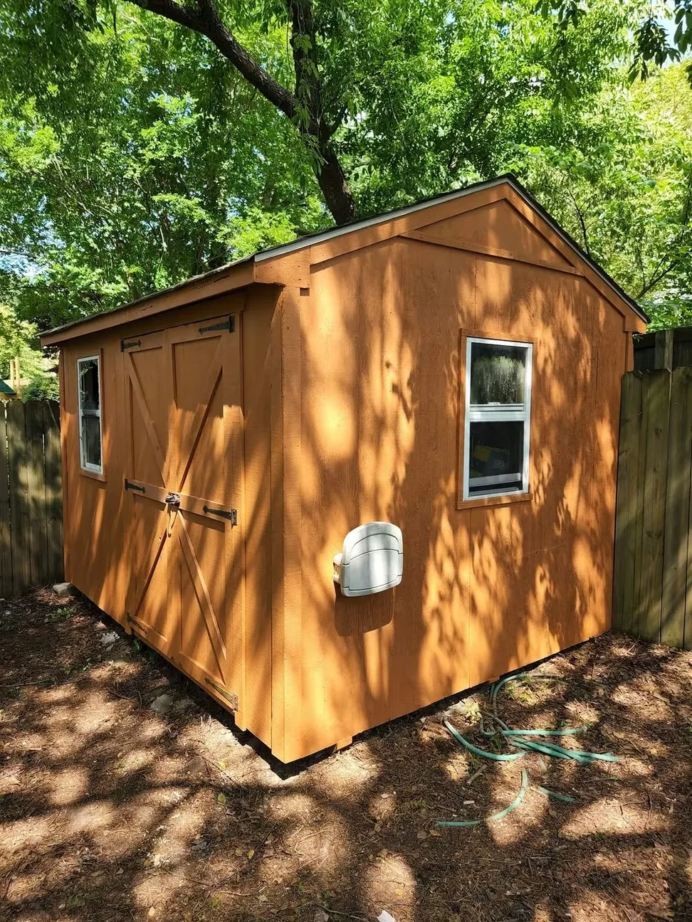 Backyard storage shed after staining, the weathered board-and-batten siding and barn doors finished in warm cedar