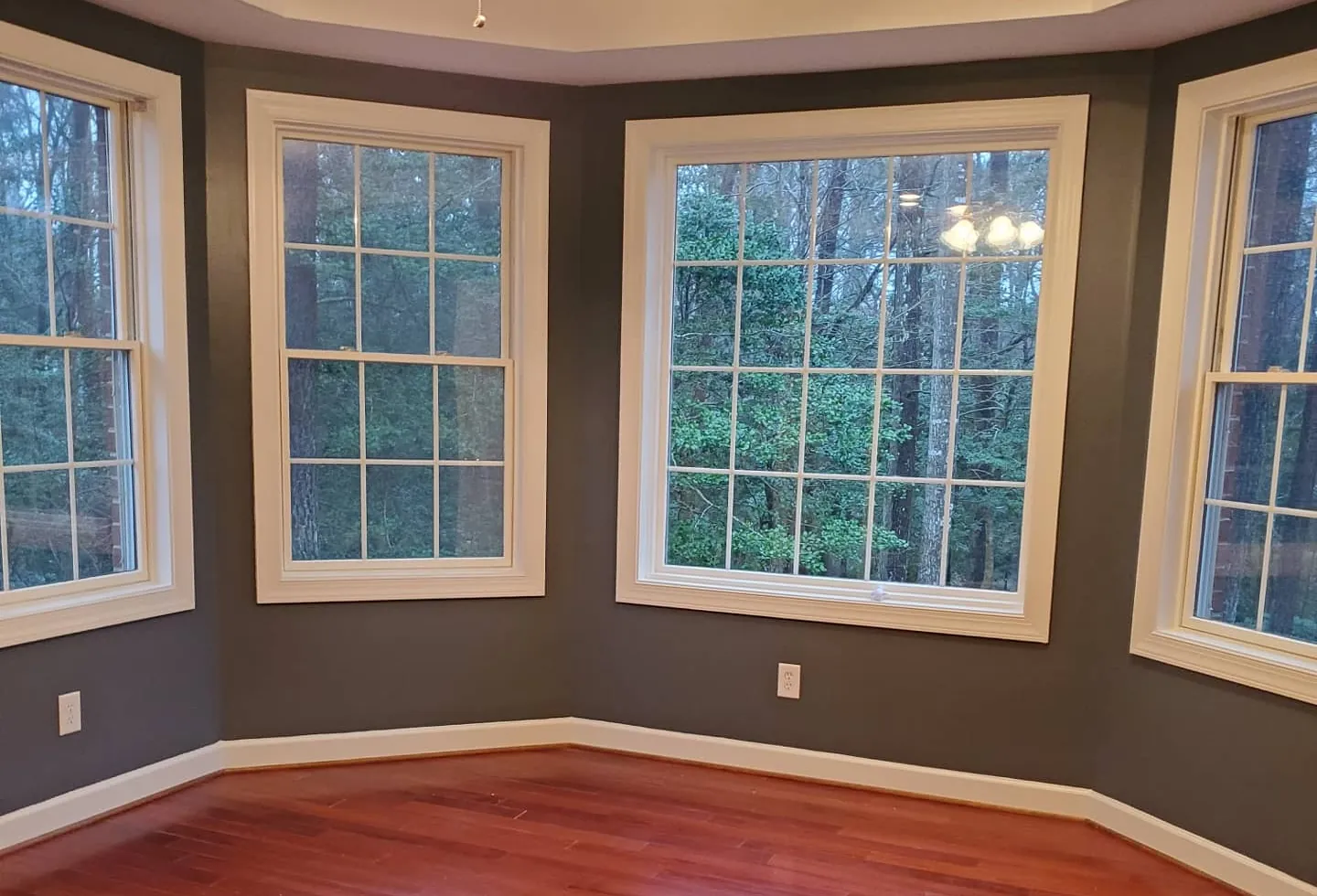 Empty dining room with dark gray-green walls, white window trim and cherry hardwood floors